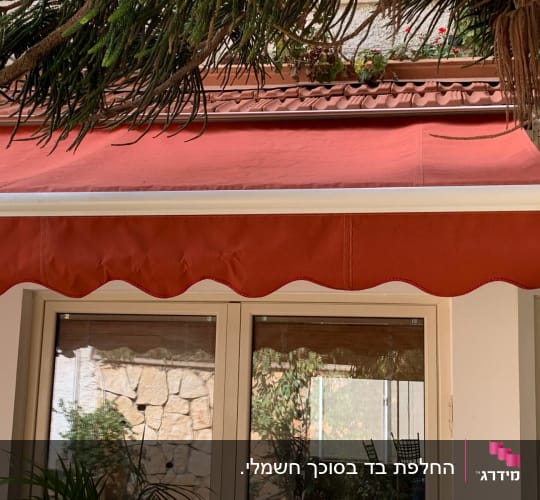 סוכך זרועות מתקפל בגוון טרקוטה מותקן מעל חלונות בית
